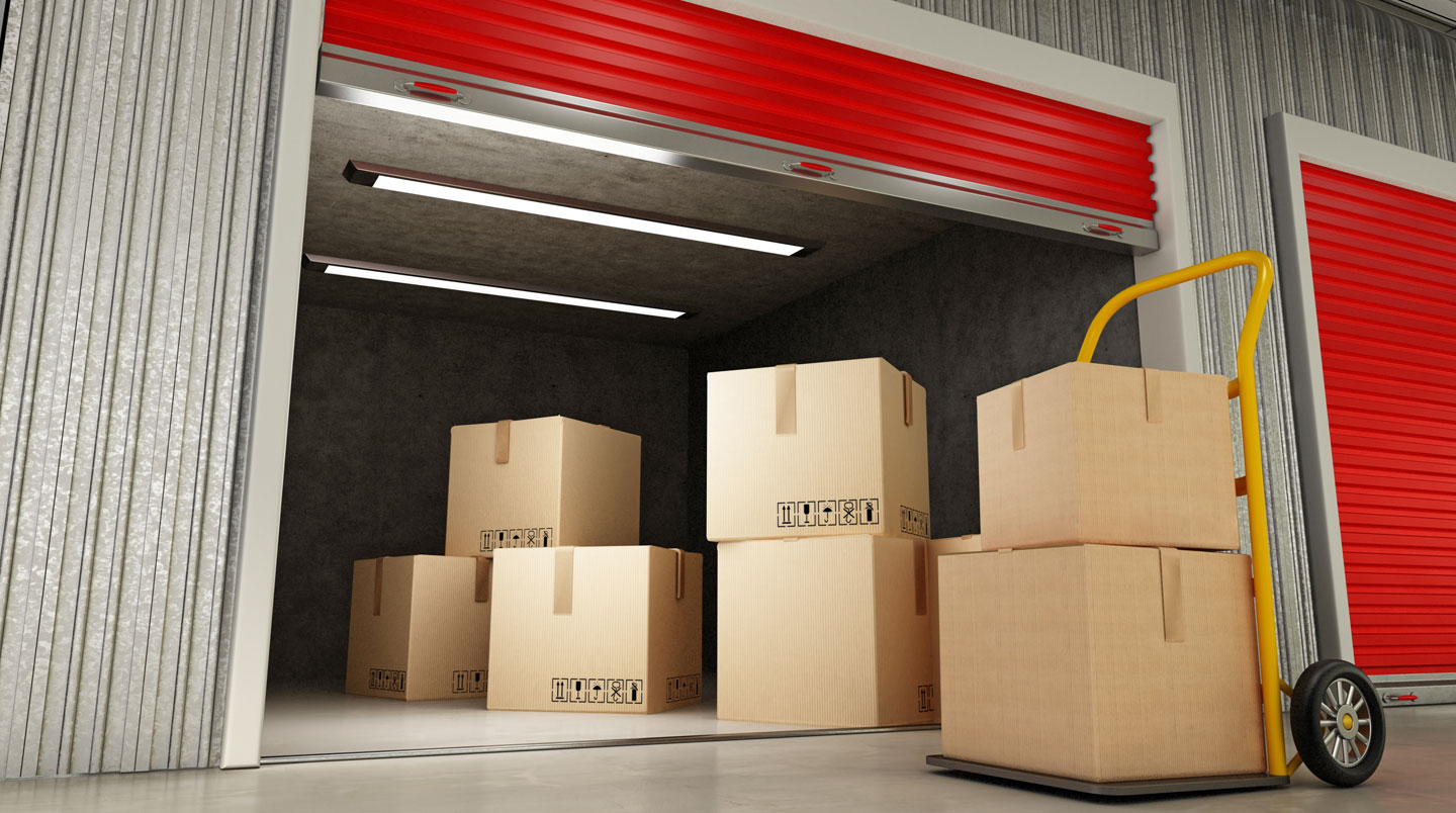 Box de stockage ouvert contenant cartons empilés, meubles protégés et chariot de manutention sur sol béton